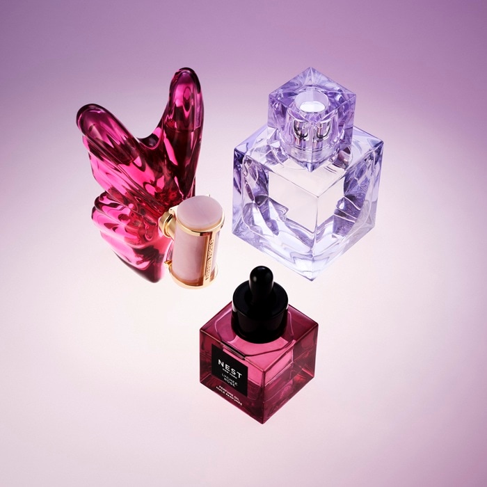Pe un fundal gradient mov, descoperiți o gamă de sticle de parfum, fiecare cu forme și nuanțe unice, de la cristal transparent la roz intens, oferind un parfum pentru fiecare femeie de Ziua Femeii.