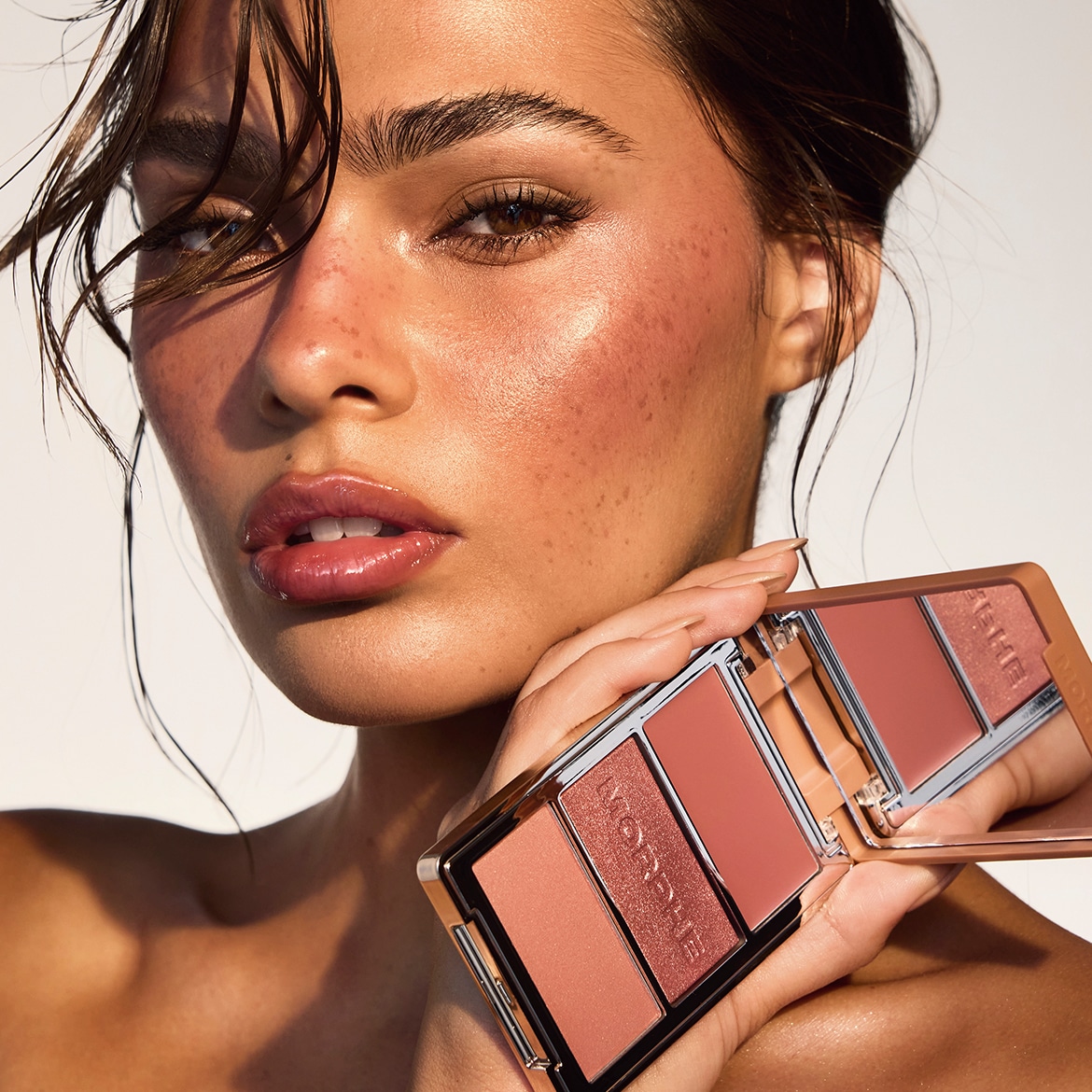 Prim-plan al unui model care ține o paletă de blush Morphe cu finisaje mate și sidefate, în nuanțe de roz și piersică.