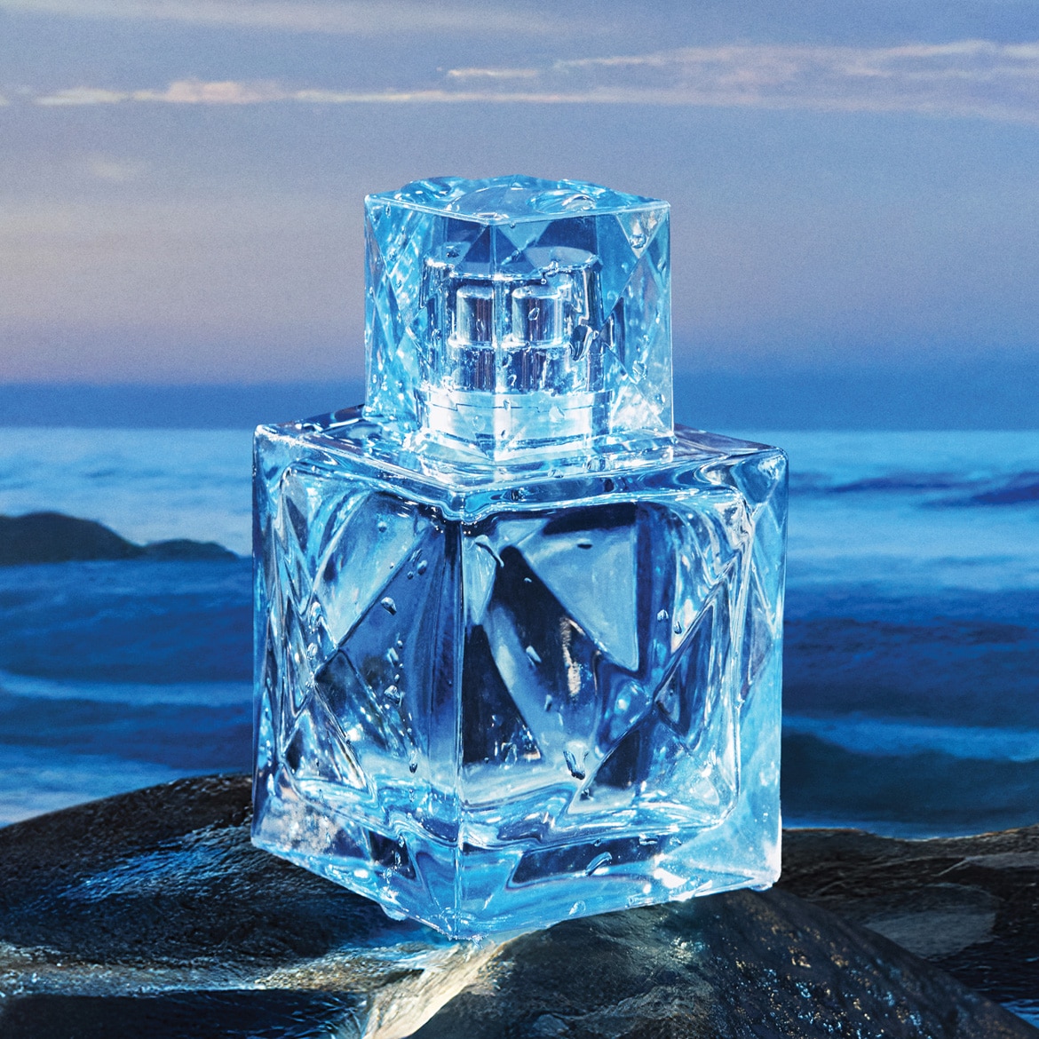 Un flacon de parfum din sticlă albastră, cu un design geometric, stă pe o stâncă umedă, cu picături de apă pe suprafața sa, având în fundal o mare agitată sub un cer înnorat.