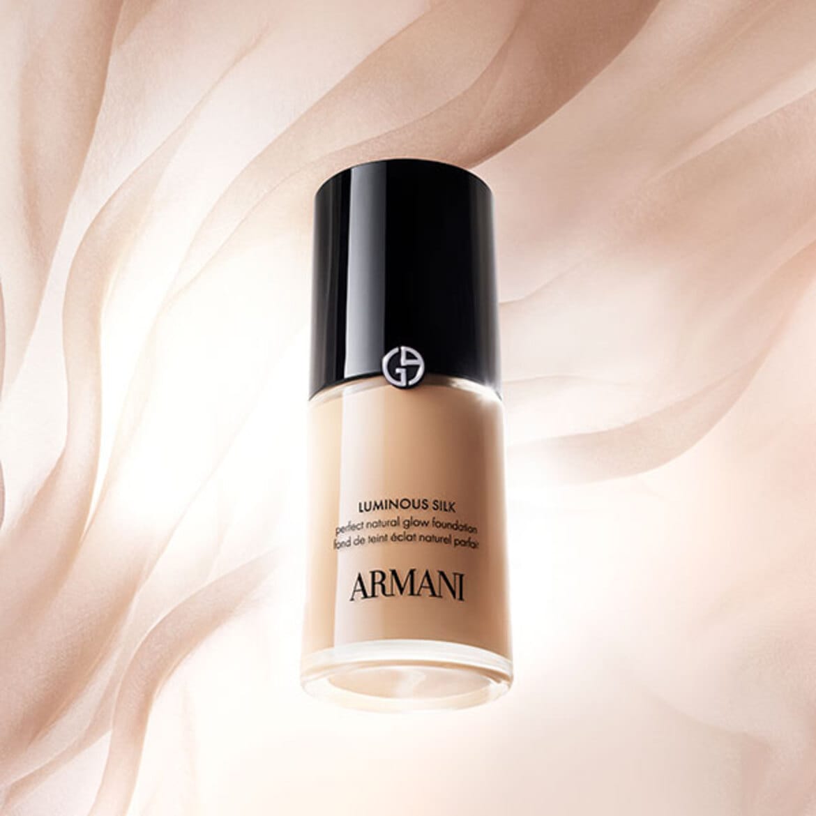 Sticlă de fond de ten Armani Luminous Silk, cu capac negru lucios, fotografiată pe un fundal bej cu textură fluidă.