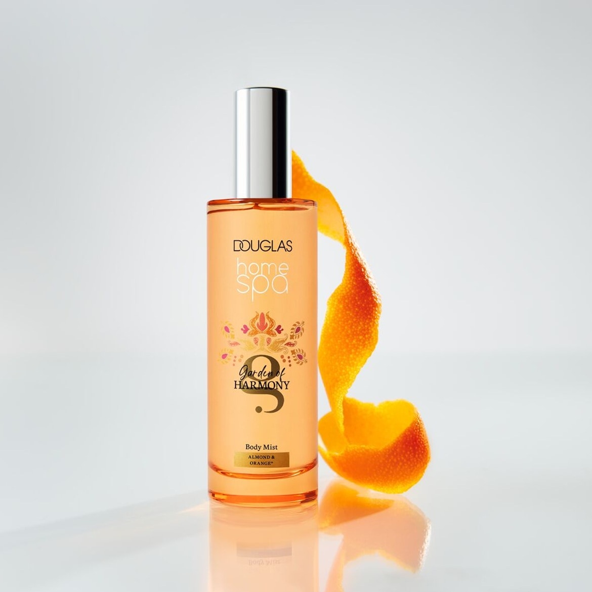 Douglas Home Spa Garden of Harmony Body Mist, cu o nuanță aurie, este prezentat într-o sticlă transparentă, cu un capac argintiu, alături de o coajă de portocală, sugerând o aromă proaspătă de citrice.