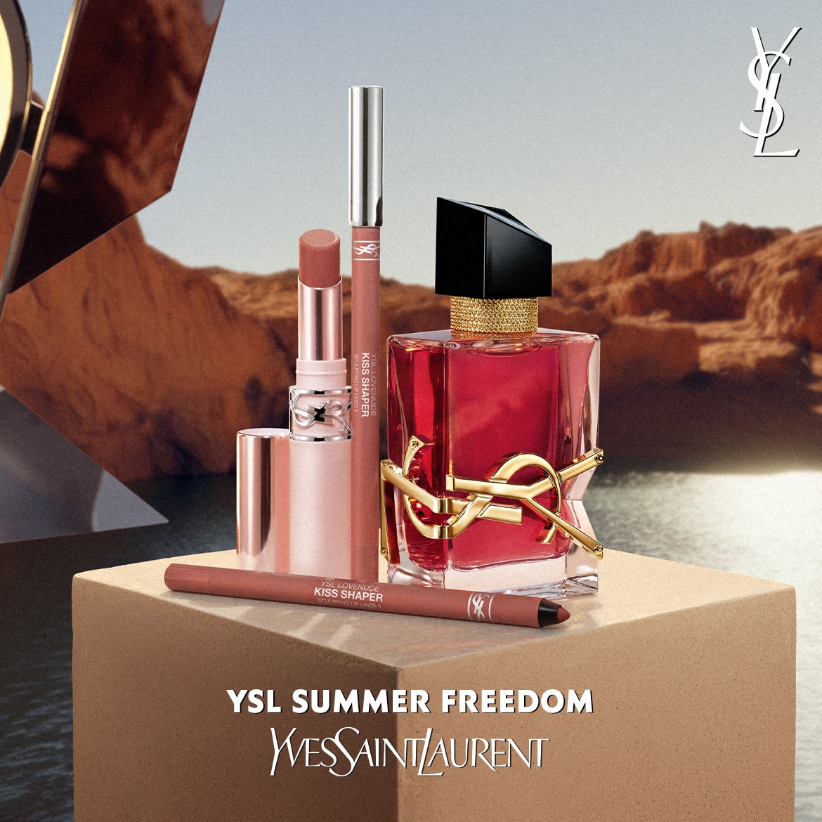 Set de produse de beauty YSL Summer Freedom: parfum, ruj, gloss și creion de buze în nuanțe nude, pe fundal deșertic.
