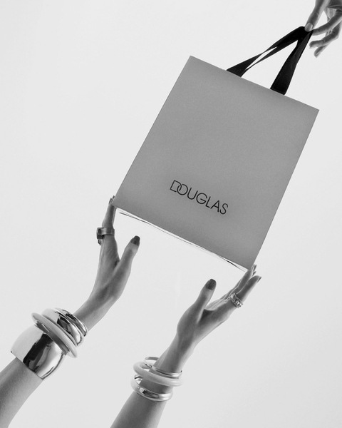 Două mâini ridică o geantă de cumpărături Douglas, accesorizată cu brățări elegante.