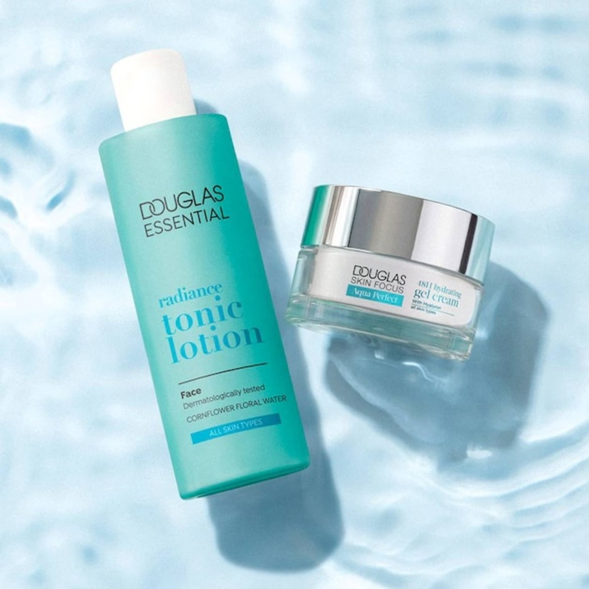 Setul Douglas Essential Radiance Tonic Lotion și Douglas Skin Focus Aqua Perfect 48H Hydrating Gel Cream, ambele în ambalaje turcoaz și alb, sunt așezate pe o suprafață albastră, cu reflexii de apă.