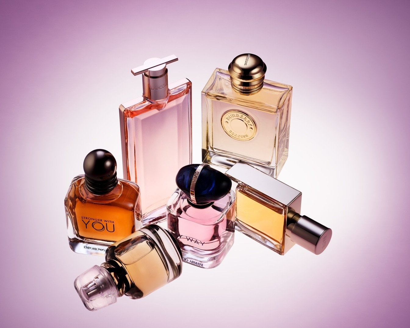 O colecție de sticle de parfum în forme și culori variate, inclusiv roz, auriu și ambra, este expusă pe un fundal mov în degrade, perfect pentru Ziua Femeii.