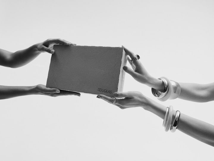 Două perechi de mâini își înmânează un pachet marca Douglas, sugerând un cadou sau o livrare.