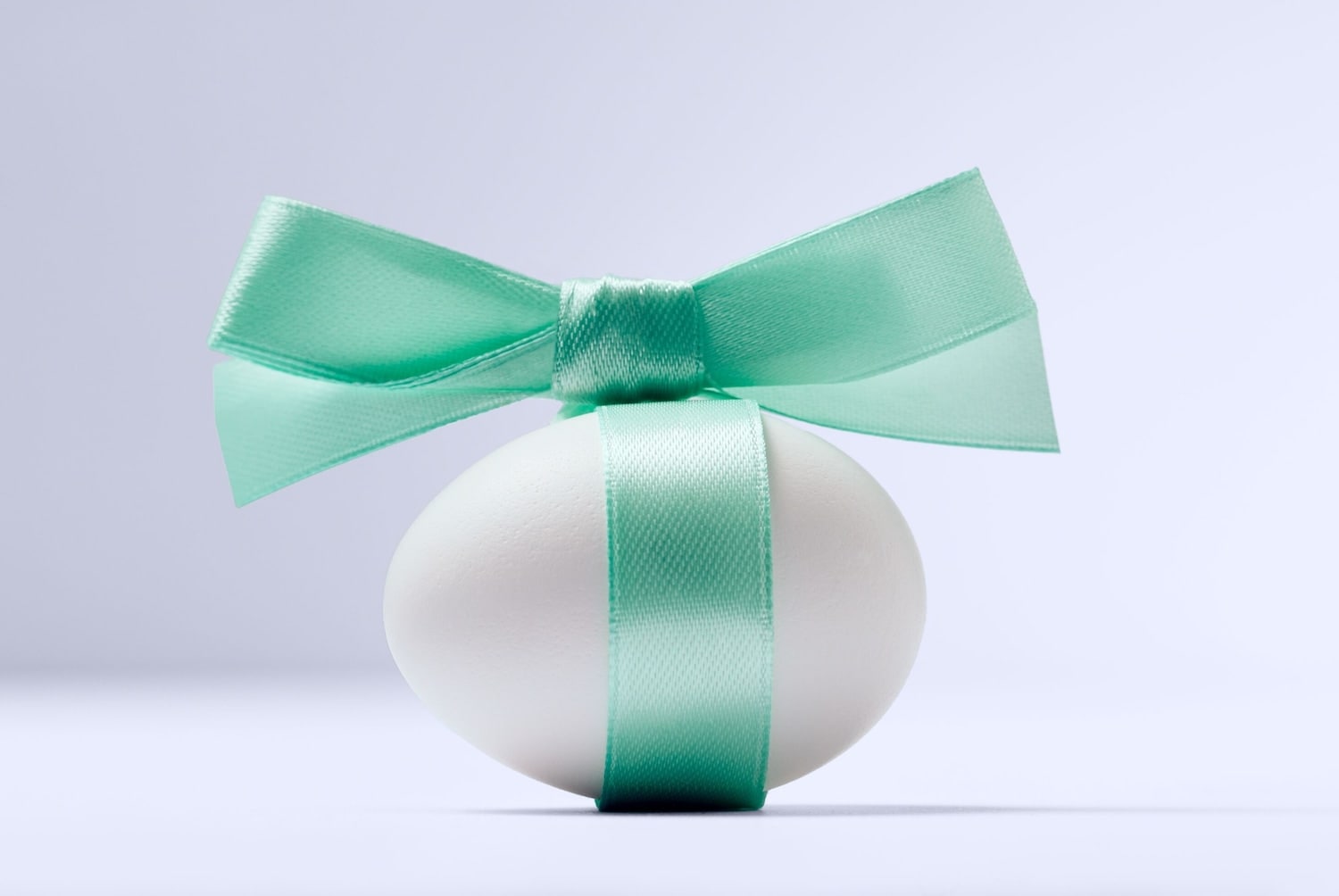 Un ou alb de Paște este înfășurat cu o panglică verde deschis și o fundiță.